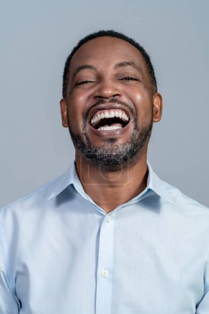 Portrait of a black adult male wearing a light blue dress shirt laughing hysterically