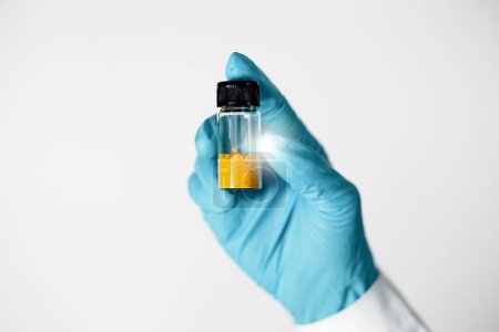 Foto de El primer plano de la mano de Scientist muestra un sólido naranja en un frasco de vidrio compuesto de curcumina de extracción y aislamiento en el laboratorio. Sustancias curcumina se utilizan para productos farmacéuticos, medicamentos. - Imagen libre de derechos