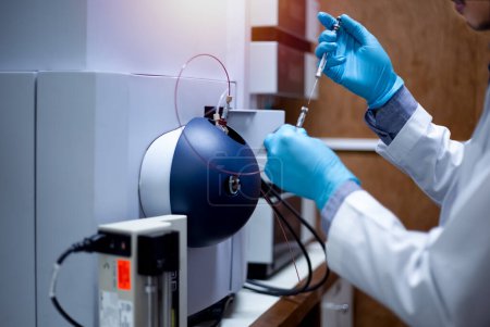 Foto de Científico inyecta muestras con micro jeringas en el espectrómetro de masas TOF para su análisis en el laboratorio. - Imagen libre de derechos