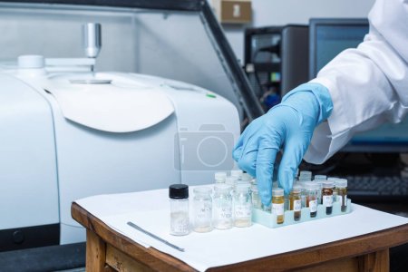 Photo for A hand of scientists arrange vials of samples in order before analysis with Fourier Transform Infrared Spectroscopy FTIR Instrument. Samples are analysed to identify the chemical identity. - Royalty Free Image