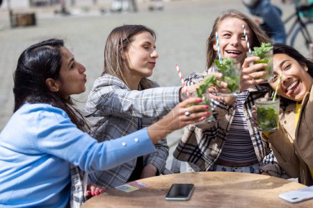 Photo for May 21, 2021, Antwerp, Belgium, Four attractive young woman of mixed race toasting with a cocktail outdoor in the city center after the reopening of bars closed for corona or covid-19 restrictions - Royalty Free Image