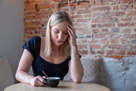 Traurig müde junge Frau mit einem Kaffee in einem Café berühren Stirn mit Kopfschmerzen Migräne oder Depressionen, verärgert frustrierte Mädchen mit Problemen fühlen sich gestresst Abdeckung weinen Gesicht mit der Hand leiden