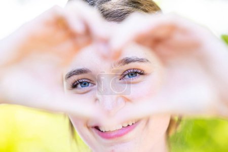 Photo for Close up image of smiling woman out in nature making a heart shape with hands. Pretty joyful caucasian woman laughing at camera outside. Healthy lifestyle, self love and body care concept. High - Royalty Free Image