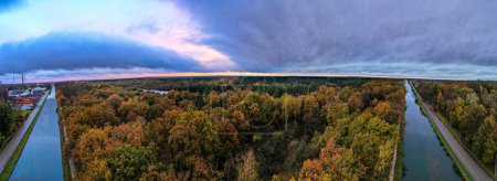 Photo for Immerse yourself in the vibrant tapestry of autumn as the camera captures an enchanting aerial view of a river or canal flowing through the woods, adorned with colorful fall foliage, all set against a - Royalty Free Image