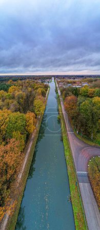 Photo for Immerse yourself in the vibrant tapestry of autumn as the camera captures an enchanting aerial view of a river or canal flowing through the woods, adorned with colorful fall foliage, all set against a - Royalty Free Image