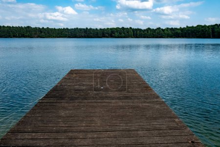 Mole, or pier, on the lake. Wooden bridge in forest in spring time with blue lake. Lake for fishing with pier. sunny blue sky with some fluffy clouds. High quality photo