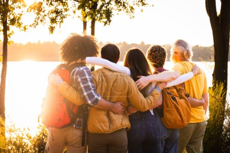 Experience the beauty of connection and natures splendor in this heartwarming image. Young people with backpacks stand close, sharing an embrace while admiring the breathtaking sunset view over the