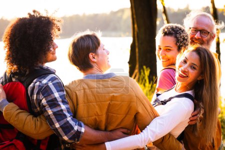 Photo for Celebrate the richness of diversity and the magic of natures canvas in this captivating scene. A multiracial group of young people with backpacks stand close, sharing an embrace while admiring the - Royalty Free Image