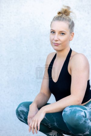 Photo for Capture the essence of an active break with this footage. A fit young sporty girl, with her long blonde hair flowing, sits gracefully on the ground. Clad in a stylish black and blue sports top and - Royalty Free Image