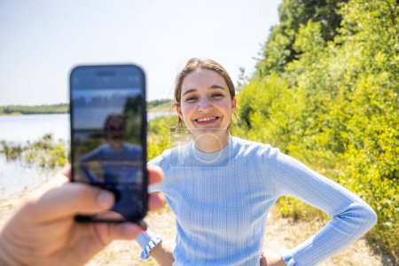 Photo for Experience the authentic connection as a male hand holds a smartphone to capture a candid moment of his attractive millennial girlfriend in the heart of summer. Their love story unfolds against the - Royalty Free Image