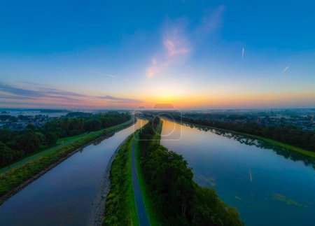 Capture the serene beauty of dawn as the sun peeks under a steel-blue sky, its golden rays reflecting off two tranquil waterways, creating a breathtaking spectacle of nature.Dawns Reflection: Sunlit
