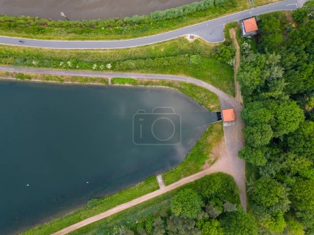 Photo for Captured from above, this image features a tranquil pond bordered by a neatly paved road and intersecting walking paths. The lush greenery encroaching upon the paths creates a cozy nook beside the - Royalty Free Image