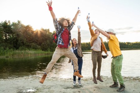 Téléchargez les photos : Capturant l'essence de la joie effrénée, cette image montre un groupe d'amis à la mi-célébration au bord du lac, l'un bondissant haut avec les bras et les jambes tendues. Leurs visages sont vivants de rire et - en image libre de droit