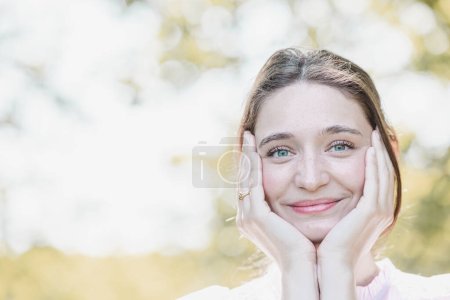Téléchargez les photos : Une jeune femme est photographiée avec un sourire radieux, les mains encadrant délicatement son visage, soulignant son expression joyeuse. Elle est placée dans un contexte lumineux et aéré avec un accent doux, transmettant la - en image libre de droit