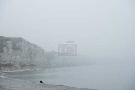 Téléchargez les photos : L'image représente une scène solitaire et contemplative le long de la côte de Fécamp en France, enveloppée de brume. Les imposantes falaises blanches se profilent en arrière-plan, leur grandeur adoucie par le linceul brumeux - en image libre de droit