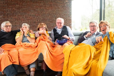 Photo for This heartwarming image captures a group of senior friends sharing a moment of joy and laughter. They are cozily tucked under a large, vibrant orange blanket, with expressions of genuine happiness and - Royalty Free Image