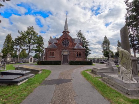 Photo for This broader view of the Mechelen Cemetery chapel encompasses the somber yet peaceful surroundings where headstones and monuments stand in quiet companionship. The chapel, with its Gothic features and - Royalty Free Image