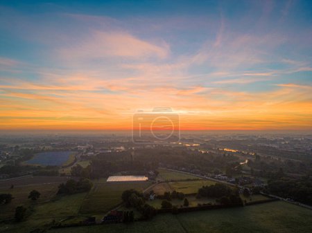 Photo for Captured at the break of dawn, this image showcases the serene beauty of the countryside bathed in the soft, warm glow of sunrise. The sky, painted in strokes of orange, pink, and blue, reflects over - Royalty Free Image