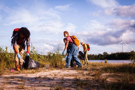 Photo for This dynamic photo captures a team of volunteers actively engaged in a lakeside conservation effort. In the foreground, a Middle-Eastern man is focused on collecting litter, while in the background, a - Royalty Free Image
