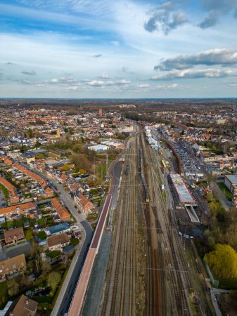 Téléchargez les photos : La photographie présente une vue aérienne étendue sur la gare de Lier en Belgique. La gare est un point focal avec plusieurs lignes de chemin de fer convergeant, entouré par l'aménagement urbain de la ville - en image libre de droit