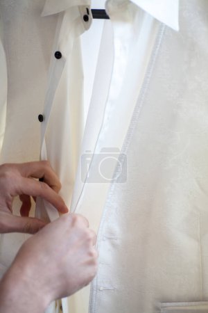 Photo for This photograph captures the meticulous process of a groom buttoning his wedding vest. The stark contrast between the crisp white shirt, the elegant ivory vest, and the black buttons establishes a - Royalty Free Image