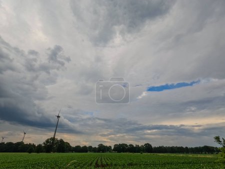 Photo for This image captures a serene agricultural landscape under a dynamic sky. A series of wind turbines stand tall on the horizon, symbolizing the fusion of traditional farming with modern renewable energy - Royalty Free Image