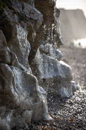 Photo for This close-up image captures the enchanting moment where fresh water trickles down a rugged cliff face to the beach below. Sunlight filters through the cascade, creating a glittering spectacle as - Royalty Free Image