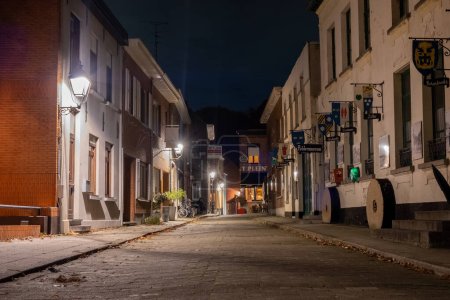Foto de Esta imagen nocturna presenta un encantador callejón en Lillo, Amberes, donde las farolas vintage proyectan un cálido y acogedor resplandor en el camino de ladrillo. Los edificios pintorescos que bordean la calle son un - Imagen libre de derechos