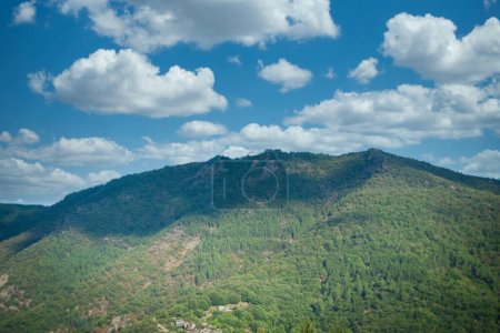 Foto de Esta fotografía de paisaje presenta las exuberantes montañas verdes de la región de Ardeche bajo un cielo salpicado de nubes de cúmulos esponjosos. El juego de la luz y la sombra a través de la ladera de la montaña crea profundidad y - Imagen libre de derechos
