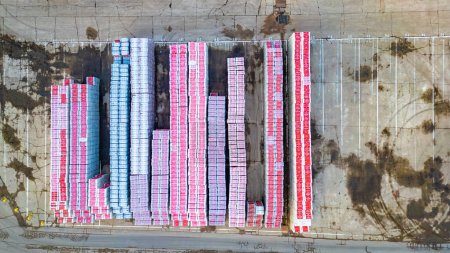Esta es una imagen aérea de arriba hacia abajo de un gran patio de almacenamiento con filas cuidadosamente organizadas de contenedores de carga de colores. Los contenedores son predominantemente de color rosa y azul, creando un patrón llamativo de