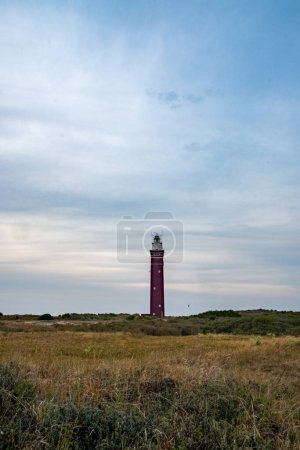Photo for This image presents a solitary red lighthouse rising above a sprawling heathland along the coast. The lighthouses stark, vertical lines contrast with the horizontal expanse of the natural landscape - Royalty Free Image
