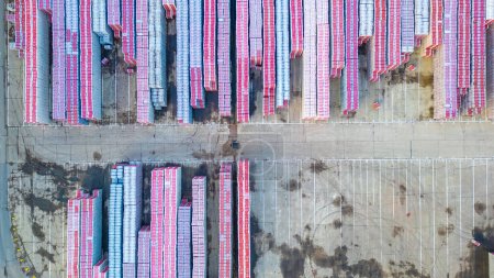Dieses Luftbild bietet einen detaillierten Blick auf ein Logistikzentrum, in dem zahllose Schiffscontainer säuberlich gestapelt sind. Die mit roten und weißen Streifen verzierten Behälter schaffen eine optisch auffällige