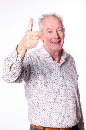This image features a joyful senior man giving a thumbs up to the viewer, his face alight with a beaming smile. His enthusiastic gesture and cheerful demeanor suggest approval, success, or a positive
