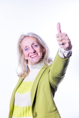 This vibrant image showcases an enthusiastic senior woman giving a thumbs up to the camera. Her bright eyes and beaming smile convey a spirit of optimism and positivity. The stylish combination of her
