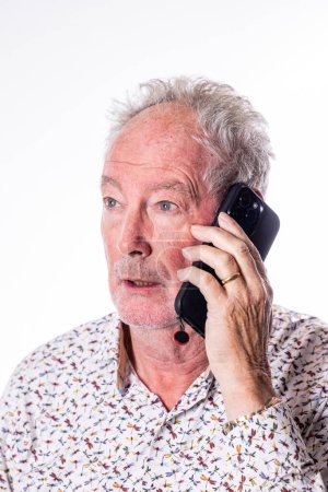 Cette image représente un homme âgé profondément engagé dans une conversation sur un smartphone moderne, son expression une de l'attention concentrée. La scène capture un moment qui reflète la tendance croissante des personnes âgées