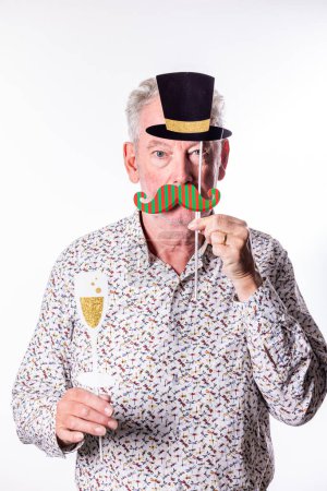 This lighthearted image showcases an elderly gentleman holding up festive party props, a paper top hat and a striped mustache, against his face, with a faux champagne flute in his other hand. His