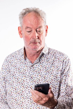 Dieses Porträt fängt einen älteren Mann ein, der stark auf sein Smartphone fokussiert ist und die zunehmende Beschäftigung älterer Generationen mit moderner Technologie repräsentiert. Sein konzentrierter Gesichtsausdruck und die sorgfältige