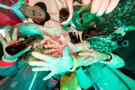 This image bursts with vibrant energy as a cluster of hands, adorned with colorful glow bracelets and sparkling attire, reaches towards the center in a show of camaraderie and celebration. The close