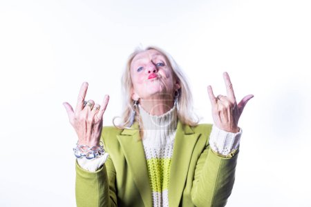 This image captures a spirited senior woman making the rock on hand gesture with both hands, her face puckered in a playful kiss. Her lively expression and the bold hand signs contrast with her