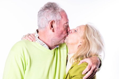 This heartwarming image depicts a senior couple sharing a tender kiss, embodying affection and long-standing love. The man, dressed in a bright green sweater, gently kisses his partner, who is clad in