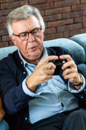 The image depicts an absorbed senior man engaged with his smartphone, possibly immersed in a game or app. His focused gaze and the intent way he interacts with the device suggests concentration and