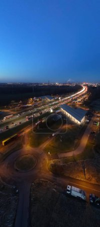 This vertical photograph offers a unique evening view of the E19 highway as it stretches towards the horizon near Halle. The road is illuminated by the streams of headlights from the bustling evening