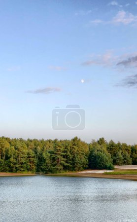 Photo for The image showcases a tranquil lake with a gentle ripple on the water surface, reflecting the waning light of dusk. A dense forest of coniferous trees forms a dark green band that separates the lake - Royalty Free Image