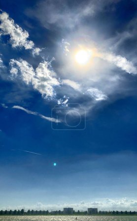 Dieses fesselnde Bild zeigt die strahlende Sonne, die in einen strahlend blauen Himmel scheint, der von einer Reihe weißer Wolken übersät ist. Die Sonnenstrahlen strecken sich aus, durchdringen die Wolken und erzeugen eine atemberaubende