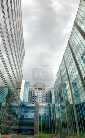 This image captures the awe-inspiring view of a corridor framed by towering glass skyscrapers reaching towards a cloudy sky. The reflective surfaces of the buildings create a visual symphony of the