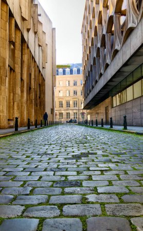 This image offers a view down a narrow cobblestone pathway flanked by contrasting architectural styles. On the left, a building with a rugged, textured facade, and on the right, a structure with a