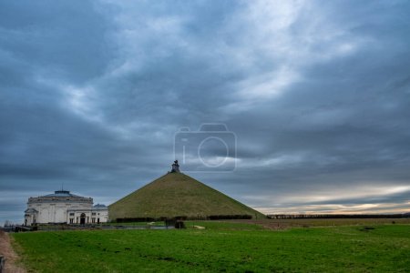 This striking landscape features the prominent Lions Mound at Waterloo, a large conical artificial hill topped with a lion statue commemorating the historic battle. To the left, the neoclassical