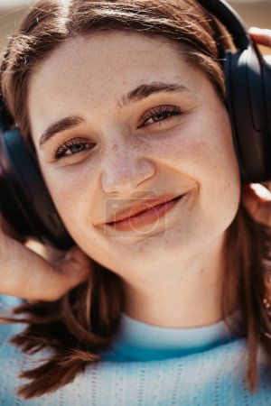 Cette image en gros plan capture une jeune femme avec un sourire subtil et heureux, portant des écouteurs sur l'oreille. L'angle du cliché accentue ses yeux détendus et fermés et la douceur de ses traits