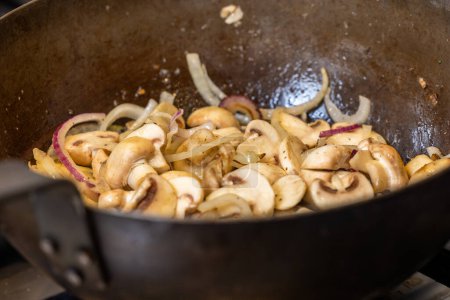 This culinary image shows sliced mushrooms and red onions being stir fried in a wok, indicative of a step in a recipe that requires sauteing vegetables to bring out their flavors. The onions are