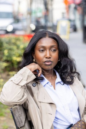 La imagen captura un momento contemplativo de una joven negra sentada en un entorno urbano. Ella mira a lo lejos, su expresión una mezcla de reflexión y serenidad. Su cabello oscuro cascadas